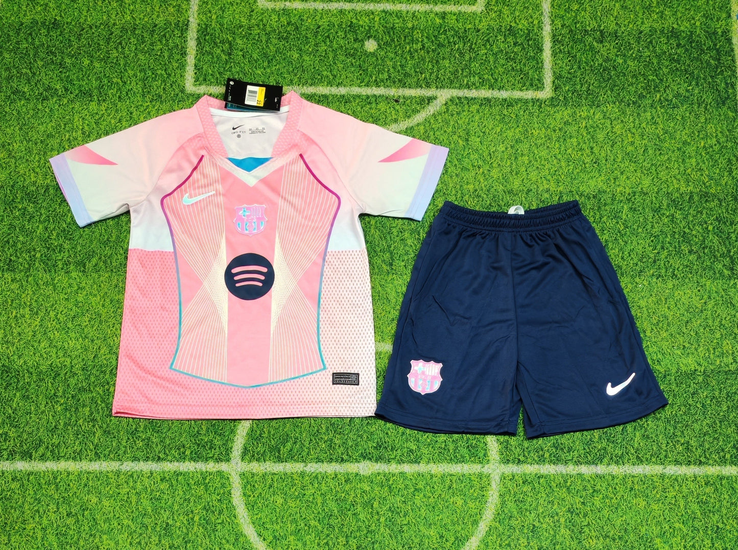 2025/26 FC Barcelona Kids Third Kit Set - Pink Jersey Navy Blue Shorts  - Pink Body White Lavender Sleeve Panels Teal V-Neck Geometric Radial Line Texture - White Nike Swoosh - FCB Pink Monochrome Crest - Spotify Navy Blue Sponsor